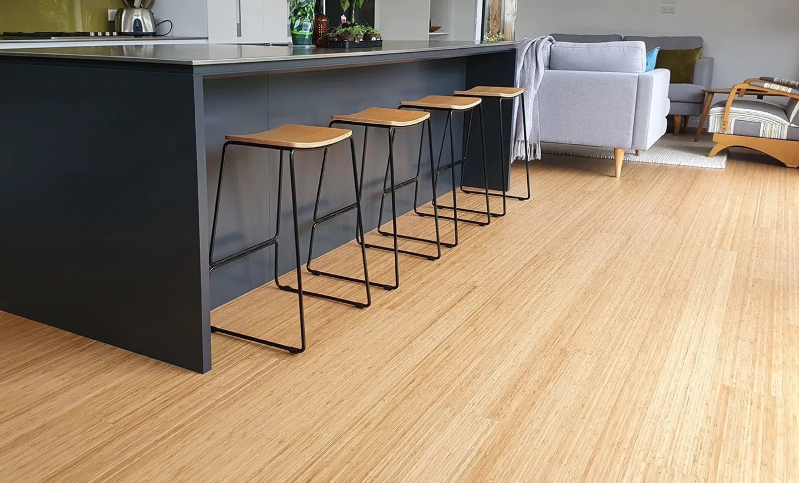 Photo of a dark grey kitchen island and stools, with a focus on the light wood grain flooring in front of it.